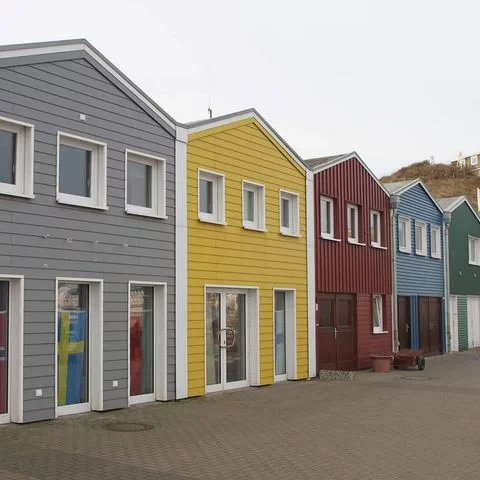 Die bunten Hummerbuden am Hafen von Helgoland – aneinandergereihte Holzhäuser in Grau, Gelb, Rot, Blau und Grün