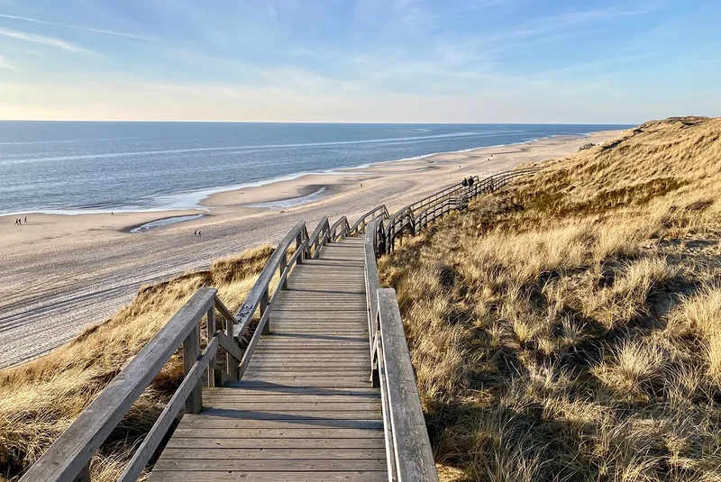 Hölzerner Bohlenweg mit Treppe führt durch die Dünen zum Sandstrand an der Nordsee, mit Blick aufs Meer