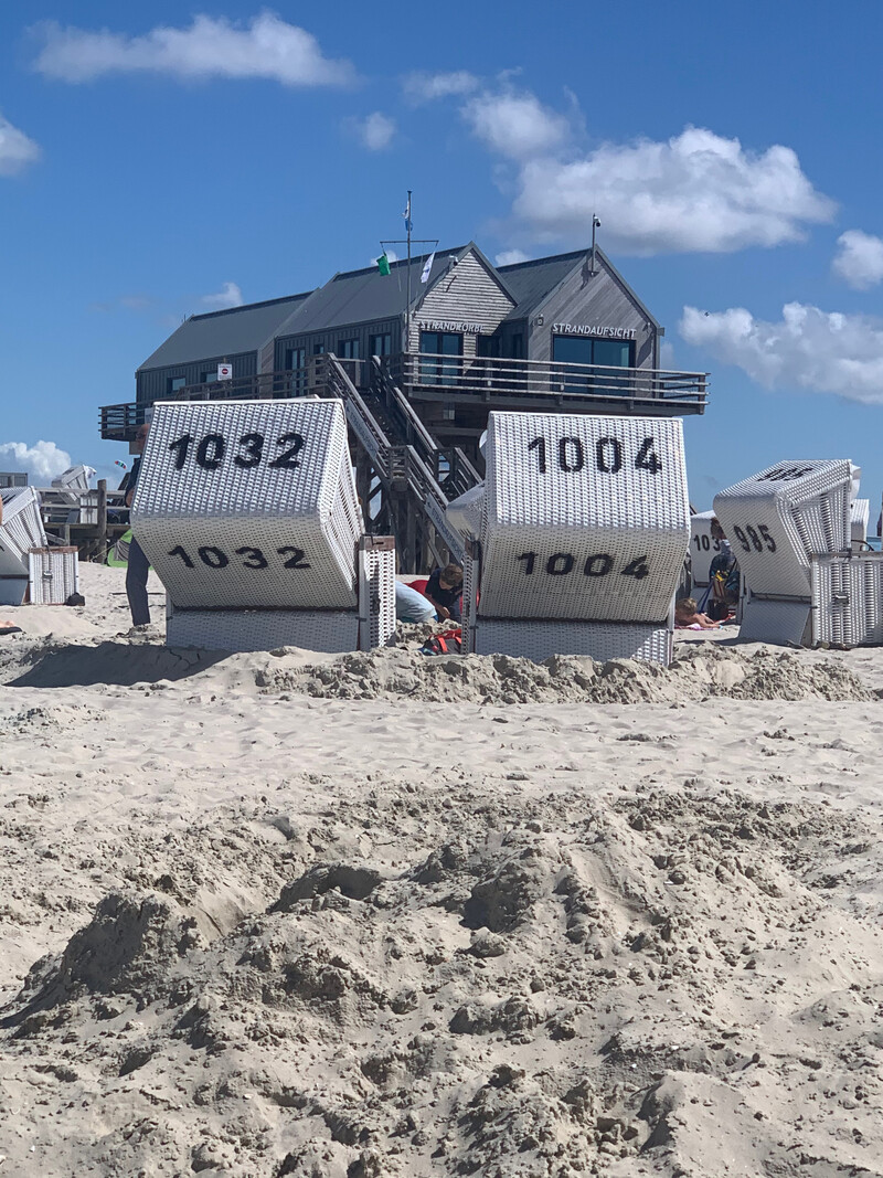 Weiße nummerierte Strandkörbe am Sandstrand von St. Peter-Ording vor dem Pfahlbau der Strandaufsicht