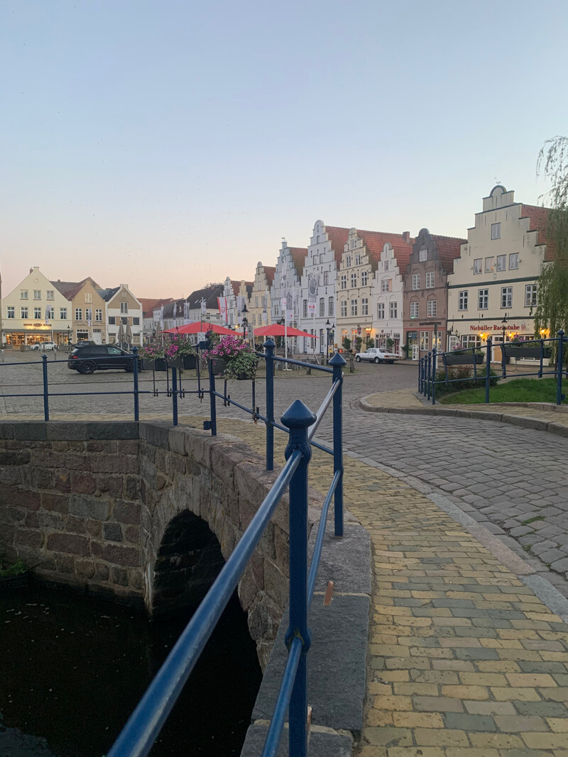 Historischer Marktplatz mit Giebelhäusern im holländischen Stil, Kopfsteinpflaster und kleiner Steinbrücke über eine Gracht in der Abenddämmerung