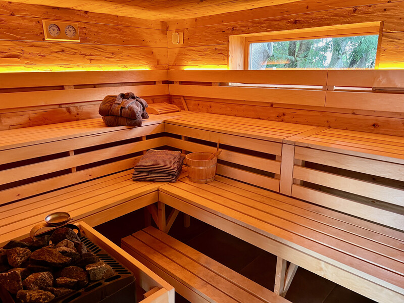 Finnische Holzsauna mit Liegebänken, Saunaofen mit Steinen, Aufgusskübel, Handtüchern und Fenster mit Blick ins Grüne
