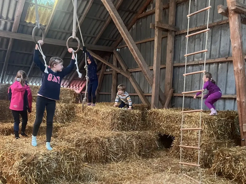 Kinder spielen während ihrer Ferien auf dem Bauernhof an der Nordsee auf dem Strohboden mit Turnringen und Strickleiter