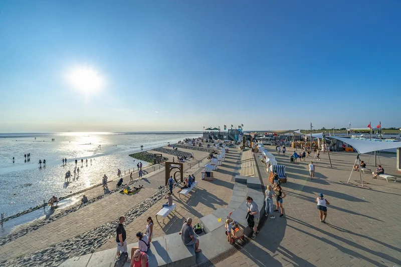 Promenade in Büsum mit Strandkörben und Sitzstufen am Wattenmeer, Urlauber laufen durchs Watt