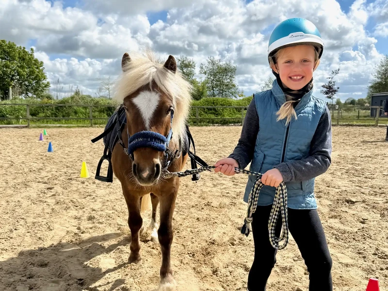 Kind führt ein Pony mit heller Mähne am Führstrick über den Reitplatz des Warfthofs Wollatz