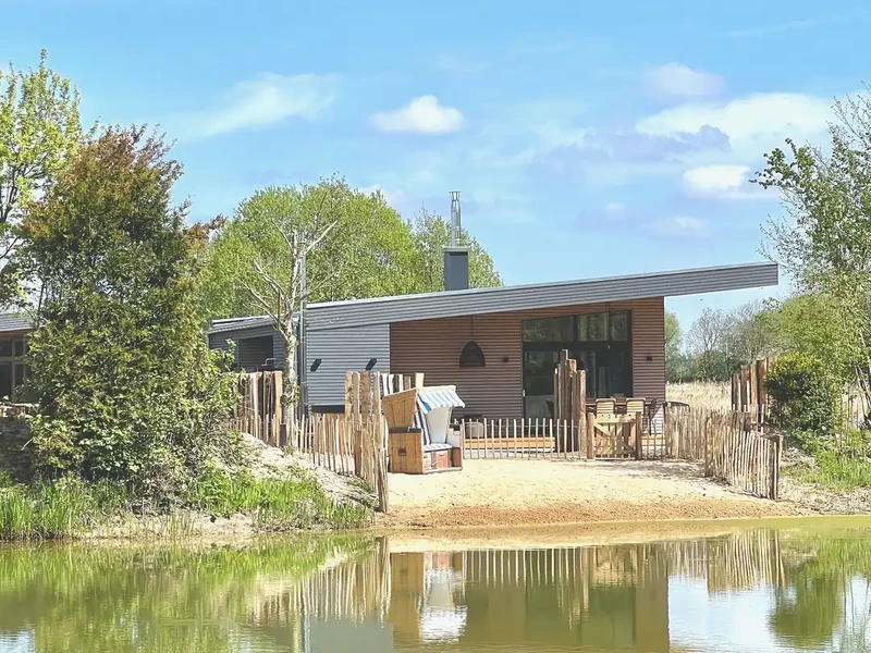 Designferienhaus StrandHaus mit Strandkorb, Holzzaun und Sandstrand am Teich des Warfthofs Wollatz