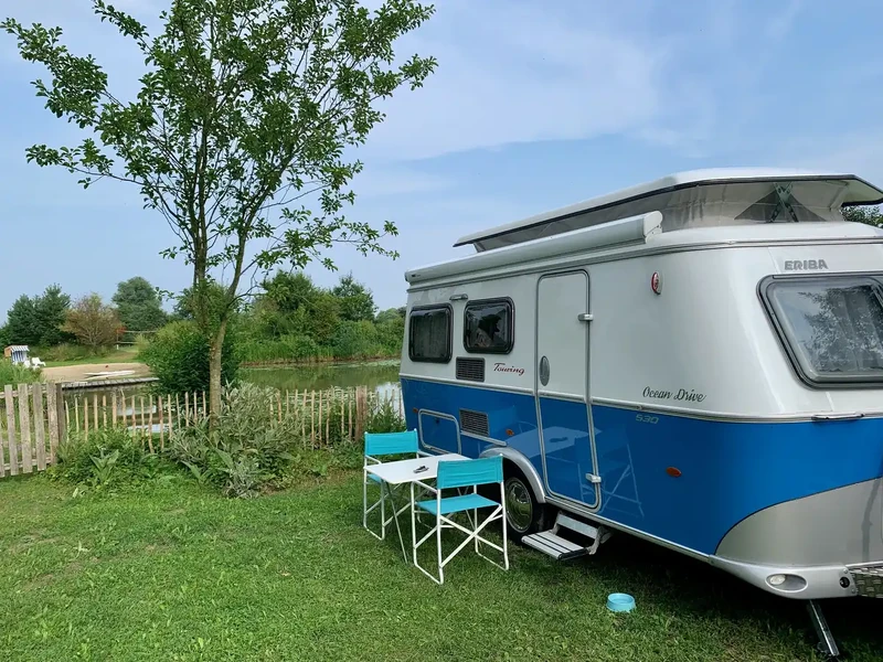 Wohnwagen mit Campingtisch und zwei Stühlen auf dem Stellplatz am Teich des Warfthofs Wollatz