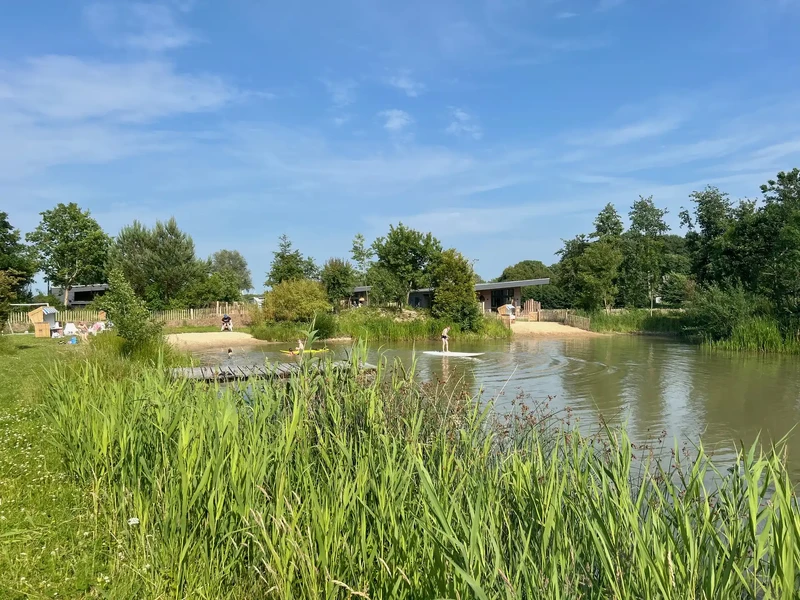 Schwimmteich auf dem Warfthof Wollatz mit Sandstrand und Strandkörben, Kinder baden und ein Junge steht auf einem SUP-Board