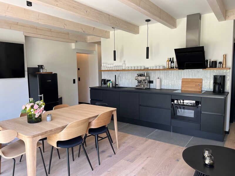 Moderne offene Küche in Anthrazit mit Holzesstisch und Stühlen, Espressomaschine, Backofen und offenem Regal; helle Holzdeckenbalken
