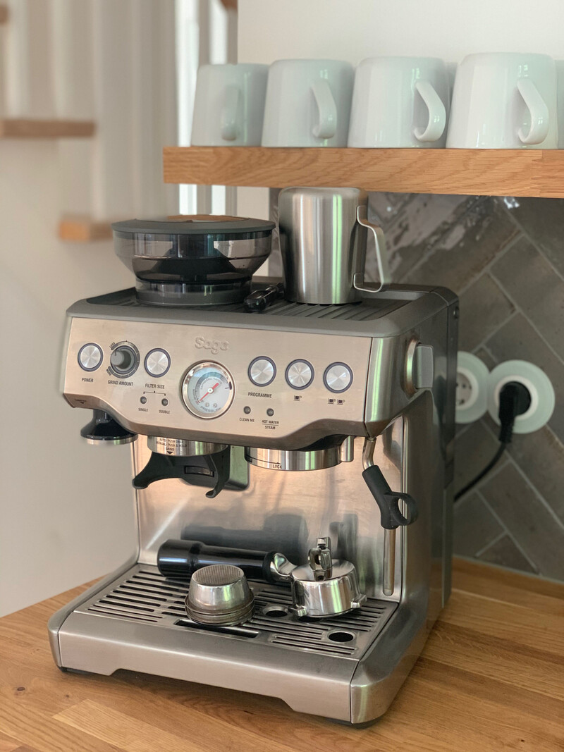 Siebträger-Espressomaschine aus Edelstahl auf Holzarbeitsplatte mit Kaffeetassen auf dem Regal