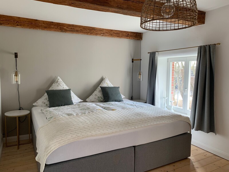 Helles Schlafzimmer mit Boxspring-Doppelbett, Nachttischen, rustikalen Holzdeckenbalken und Fenster mit Blick nach draußen