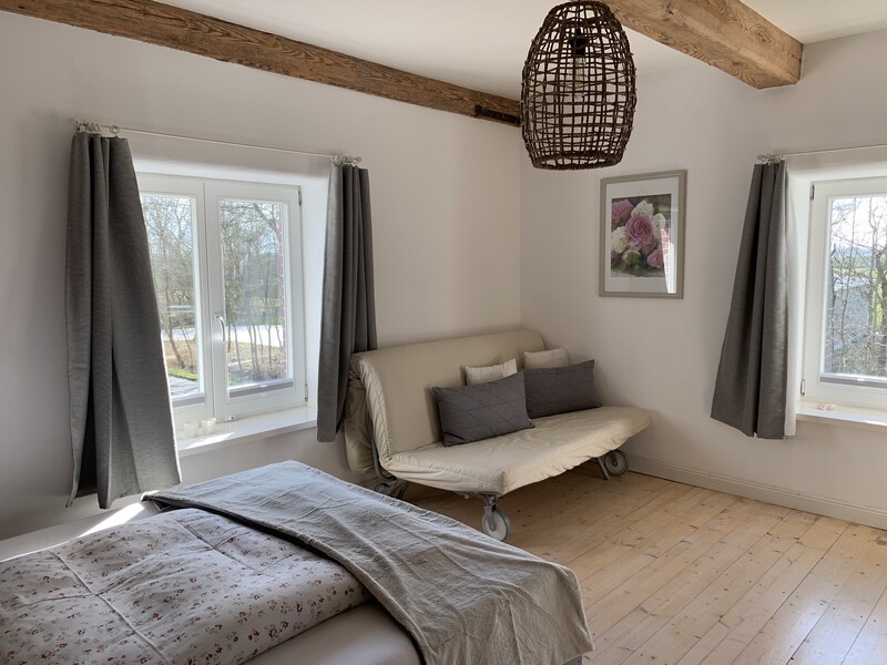 Schlafzimmer einer Ferienunterkunft mit Bett, Schlafsofa, Holzbalken und zwei Fenstern