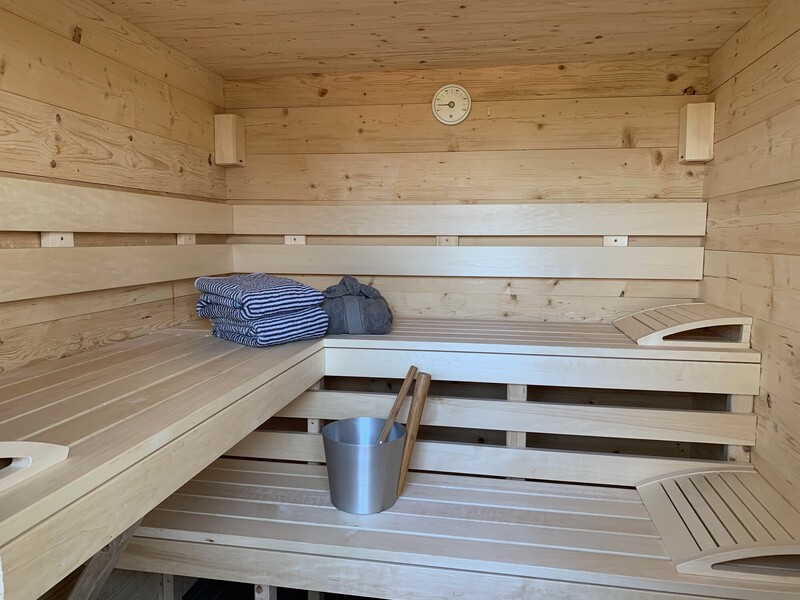 Finnische Holzsauna mit Liegebänken, Handtüchern, Saunakübel mit Kelle und Sanduhr an der Wand
