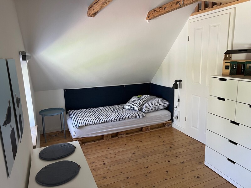 Schlafzimmer unter der Dachschräge mit Palettenbett, gestreifter Bettwäsche, Kommode und rustikalen Holzdeckenbalken