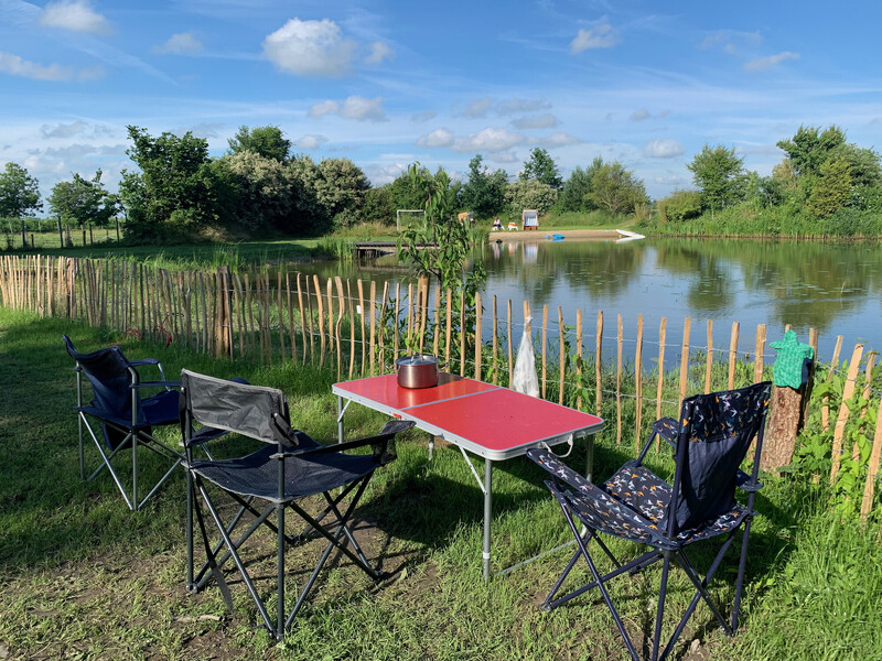 Campingplatz am Schwimmteich mit Campingtisch und Faltstühlen auf der Wiese
