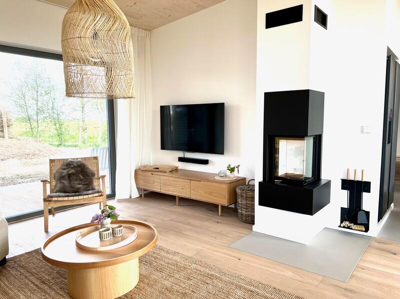 Wohnbereich eines Designhauses am Warfthof Wollatz mit Kamin, Sitzecke, Fernseher und Panoramafenster mit Gartenblick