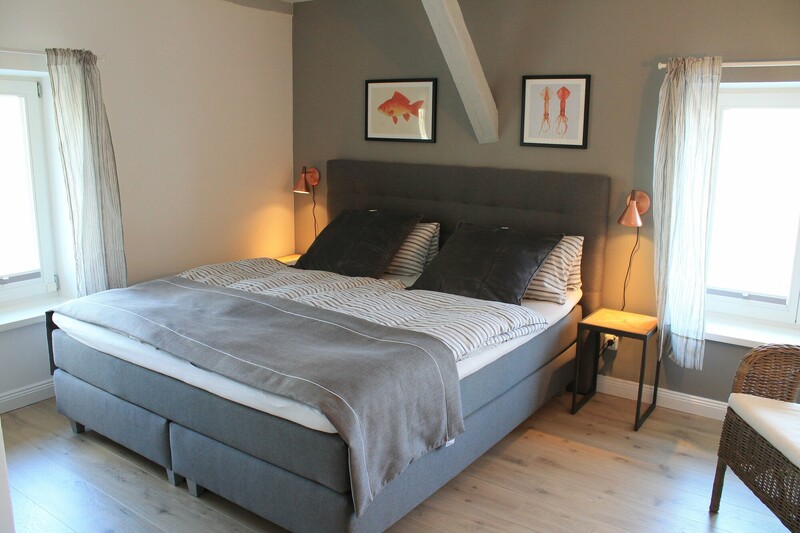 Schlafzimmer einer Ferienunterkunft mit Boxspring-Doppelbett, Nachttischen und maritimen Bildern am Warfthof Wollatz