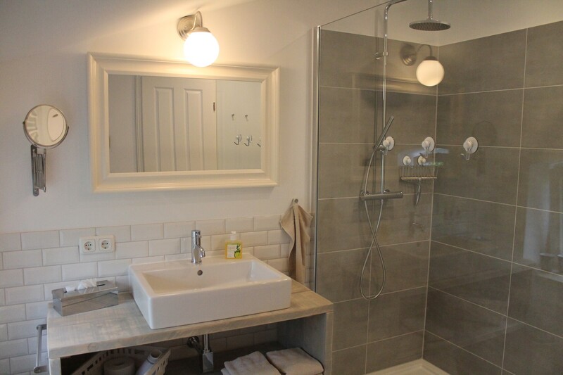 Badezimmer einer Ferienunterkunft mit Waschtisch, Spiegel und bodengleicher Dusche am Warfthof Wollatz