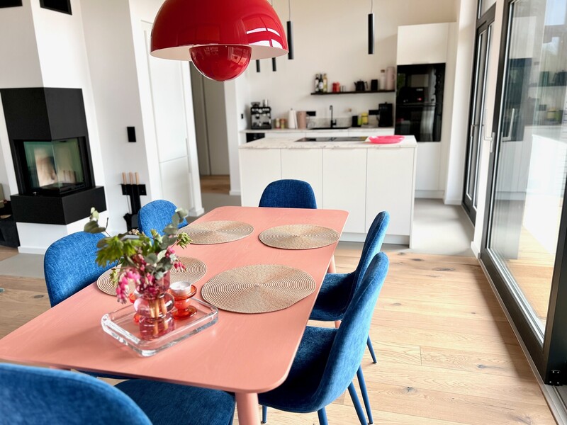 Offener Wohn-Essbereich vom Haus NordseeGut mit Esstisch, blauen Stühlen, Kaminofen und weißer Küche
