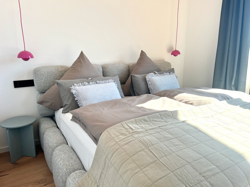 Doppelbett im Haus NordseeGut mit Polster-Kopfteil, pinken Pendelleuchten und blauem Beistelltisch
