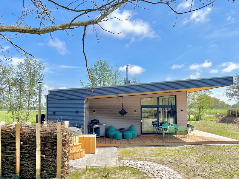 Modernes Ferienhaus Haus NordseeGut mit Flachdach, Holzterrasse und Badebottich in weiter Wiesenlandschaft