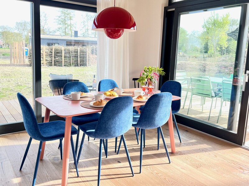 Essbereich vom Haus NordseeGut mit gedecktem Tisch, blauen Stühlen, roter Pendelleuchte und Gartenblick