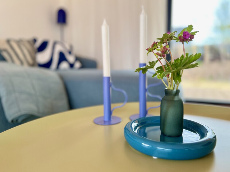 Grüne Vase mit Blumen und blaue Kerzenhalter auf gelbem Couchtisch