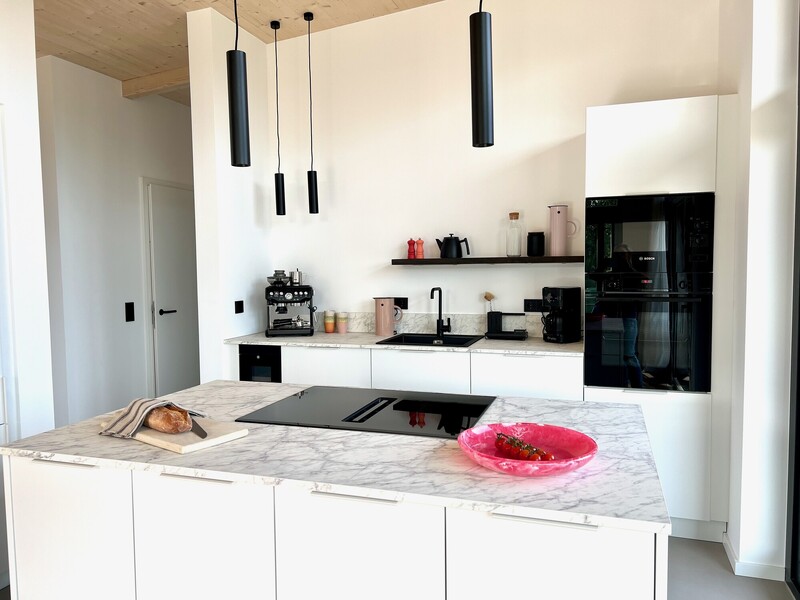 Küche vom Haus NordseeGut mit weißen Fronten, Marmor-Kochinsel, schwarzen Pendelleuchten und Backofen