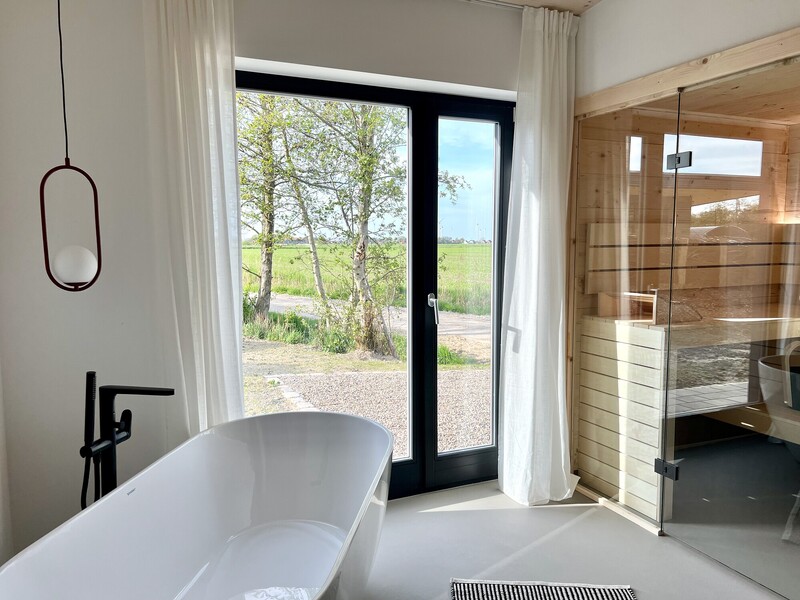 Badezimmer vom Haus NordseeGut mit freistehender Badewanne, Sauna und Panoramafenster mit Wiesenblick