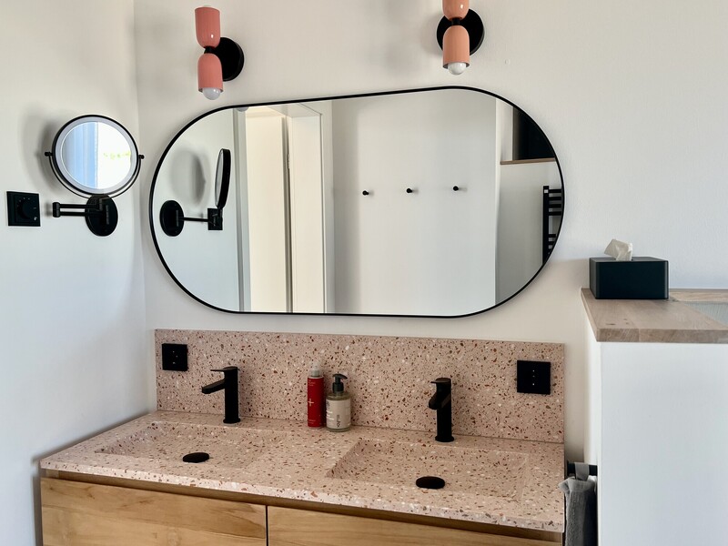 Waschtisch im Haus NordseeGut mit rosa Terrazzo-Doppelwaschbecken, ovalem Spiegel und schwarzen Armaturen