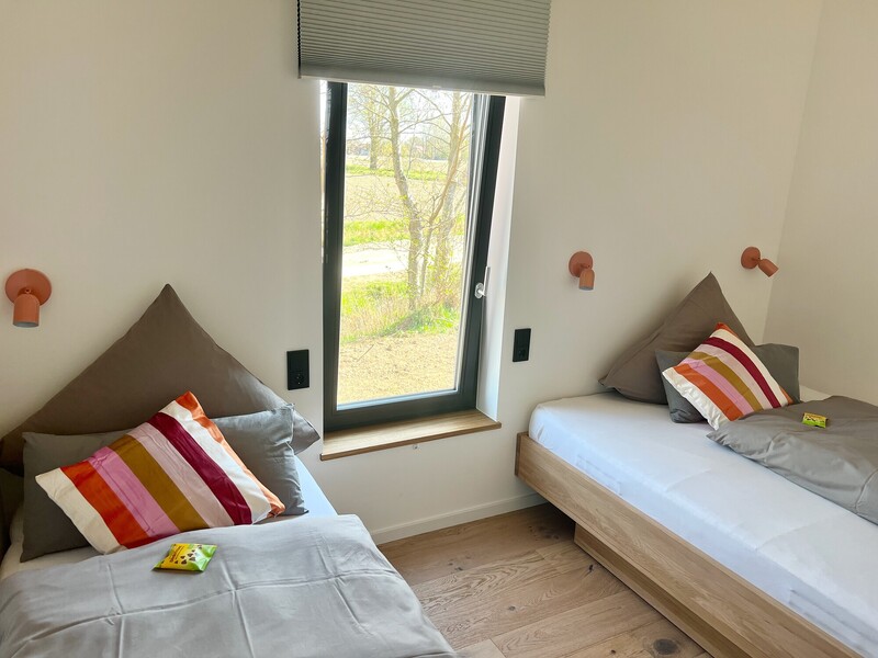Zweites Schlafzimmer im Haus NordseeGut mit zwei Einzelbetten, Wandleuchten und Fenster mit Gartenblick