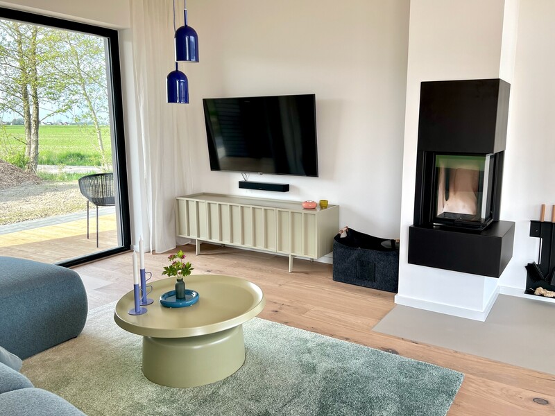Wohnzimmer vom Haus NordseeGut mit Kaminofen, Fernseher, Sideboard und Panoramafenster mit Wiesenblick