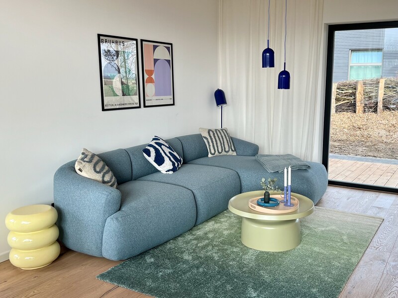 Wohnzimmer vom Haus NordseeGut mit blauem Rundsofa, grünem Teppich, Couchtisch und blauen Pendelleuchten