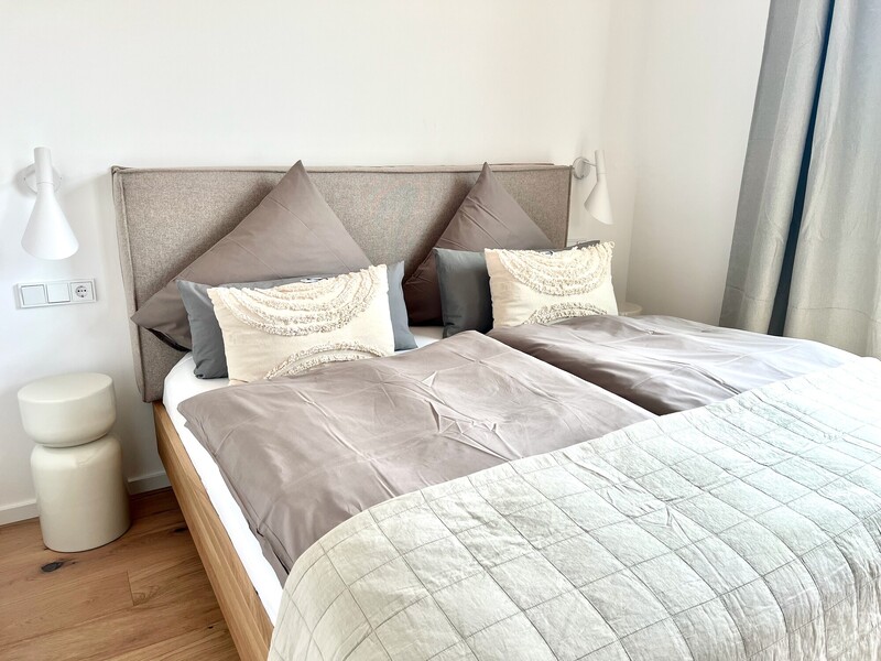 Schlafzimmer im Haus NordseeLuft mit Doppelbett, gepolstertem Kopfteil, Wandleuchten und Nachttisch