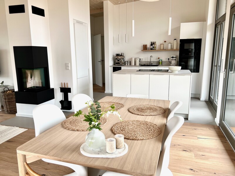 Offener Wohn-Essbereich vom Haus NordseeLuft mit Holz-Esstisch, weißen Stühlen, Kaminofen und Küche