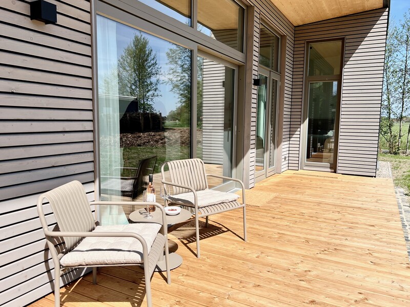 Terrasse vom Haus NordseeLuft mit zwei Loungesesseln, Beistelltisch und Holzfassade mit Blick ins Grüne