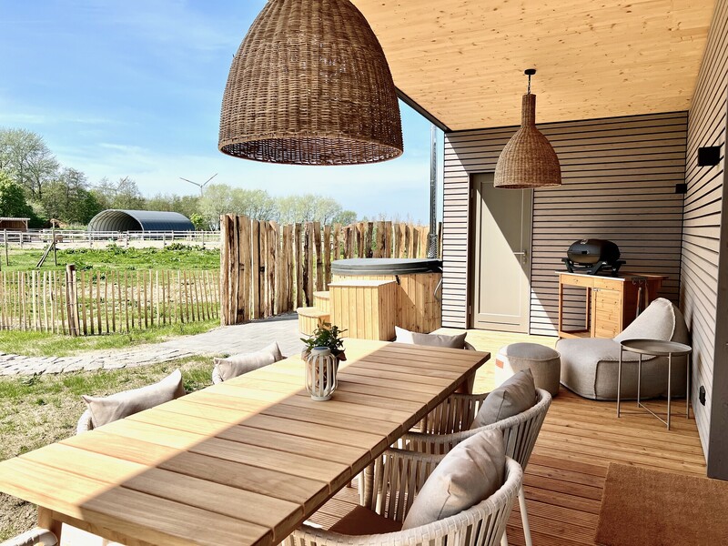 Überdachte Terrasse vom Haus NordseeLuft mit Holztisch, Rattanleuchten, Grill und Badebottich mit Feldblick
