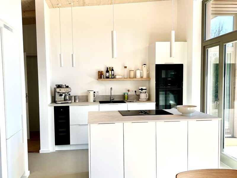 Küche vom Haus NordseeLuft mit weißen Fronten, Kochinsel, weißen Pendelleuchten und Einbaugeräten