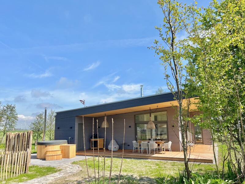 Modernes Ferienhaus Haus NordseeLuft mit Flachdach, Holzterrasse und Badebottich in weiter Landschaft