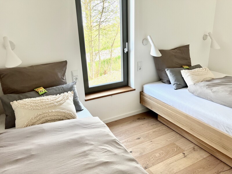 Zweites Schlafzimmer im Haus NordseeLuft mit zwei Einzelbetten, Wandleuchten und Fenster mit Naturblick