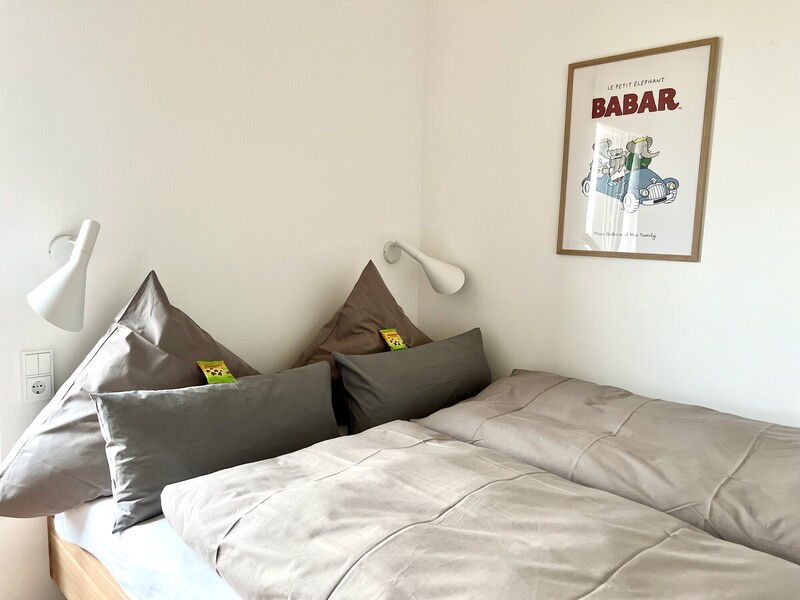 Schlafzimmer im Haus NordseeLuft mit Doppelbett, Wandleuchten und gerahmtem Poster an heller Wand
