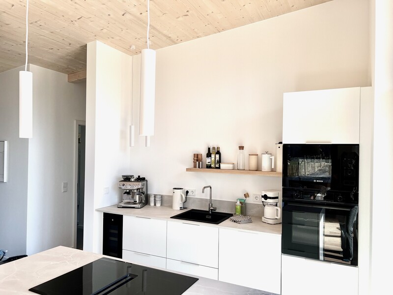 Küchenzeile im Haus NordseeLuft mit weißen Fronten, Spüle, Backofen und weißen Pendelleuchten