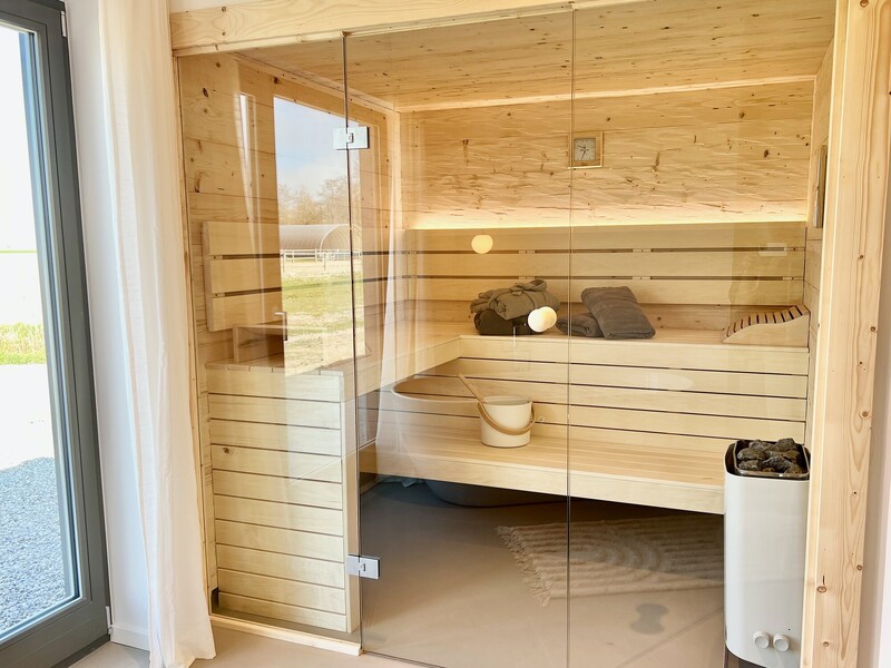 Sauna im Haus NordseeLuft mit Holzbänken, Saunaofen, Glasfront und Fenster mit Blick nach draußen