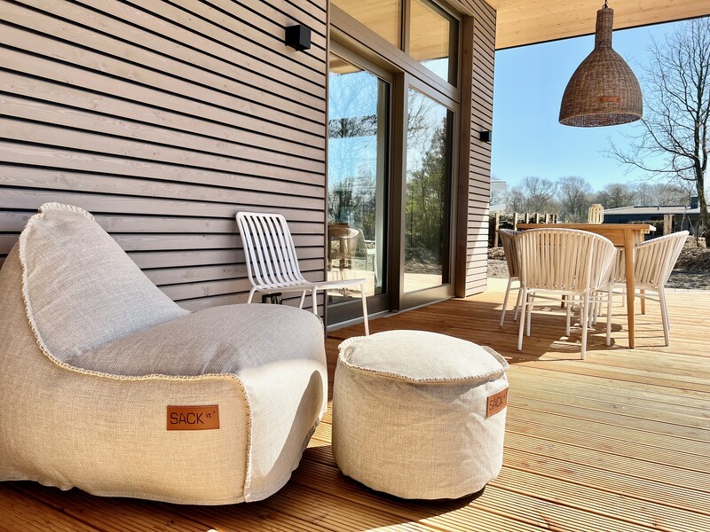 Terrasse vom Haus NordseeLuft mit beigem Sitzsack, Hocker, Esstisch und Rattan-Pendelleuchte in der Sonne