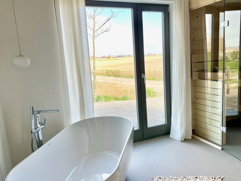 Badezimmer vom Haus NordseeLuft mit freistehender Badewanne, Sauna und Fenster mit Blick über die Felder