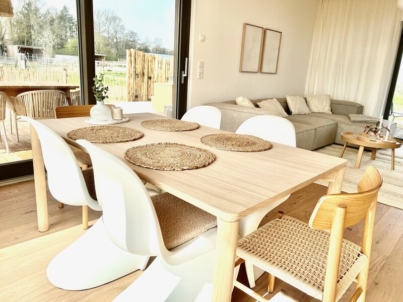Essbereich vom Haus NordseeLuft mit Holztisch, weißen Stühlen, Sofa und Fensterfront zur Terrasse