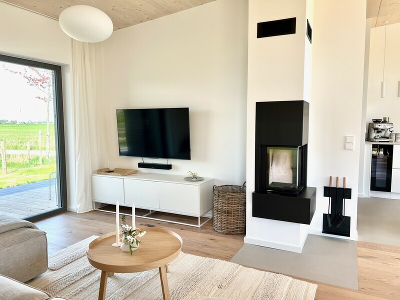 Heller Wohnraum im Haus NordseeLuft mit Kaminofen, TV-Sideboard und bodentiefem Fenster ins Grüne