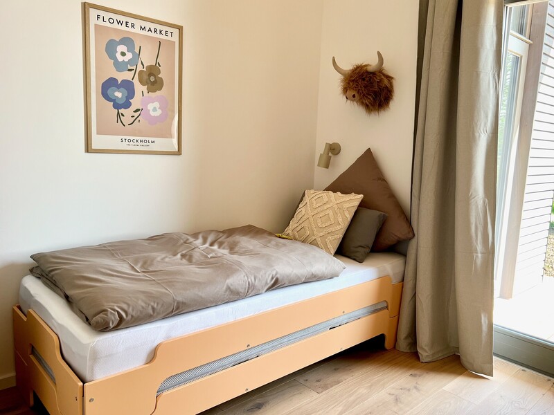 Schlafzimmer im Haus NordseeZeit mit Einzelbett, Wandleuchte, gerahmtem Poster und Fenster