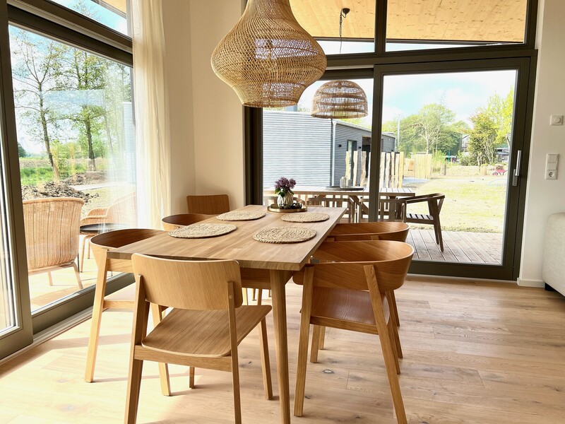 Offener Wohn-Essbereich im Haus NordseeZeit mit Holz-Esstisch, Stühlen, Kaminofen und Küche im Hintergrund