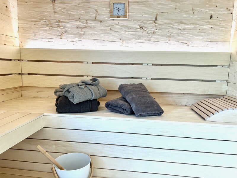 Innenansicht der Sauna im Haus NordseeZeit mit Holzbänken, Handtüchern, Aufgusskübel und Thermometer
