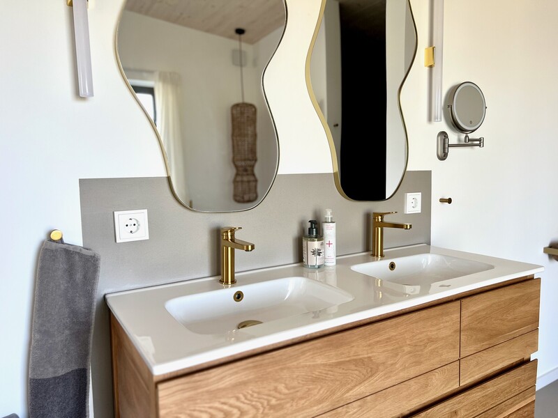 Waschtisch im Haus NordseeZeit mit Holz-Doppelwaschbecken, goldenen Armaturen und geschwungenen Spiegeln